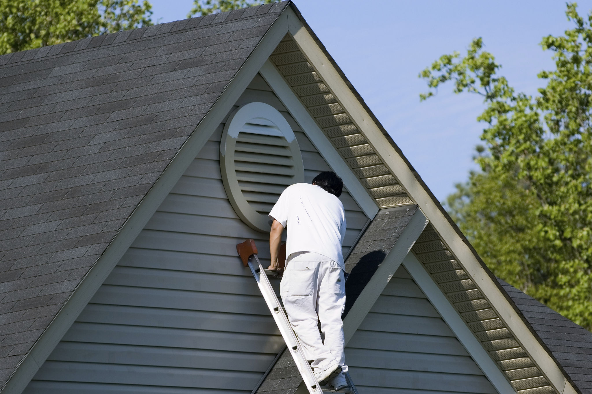 painter working at the top of an extension ladder on a two story suburban home.
