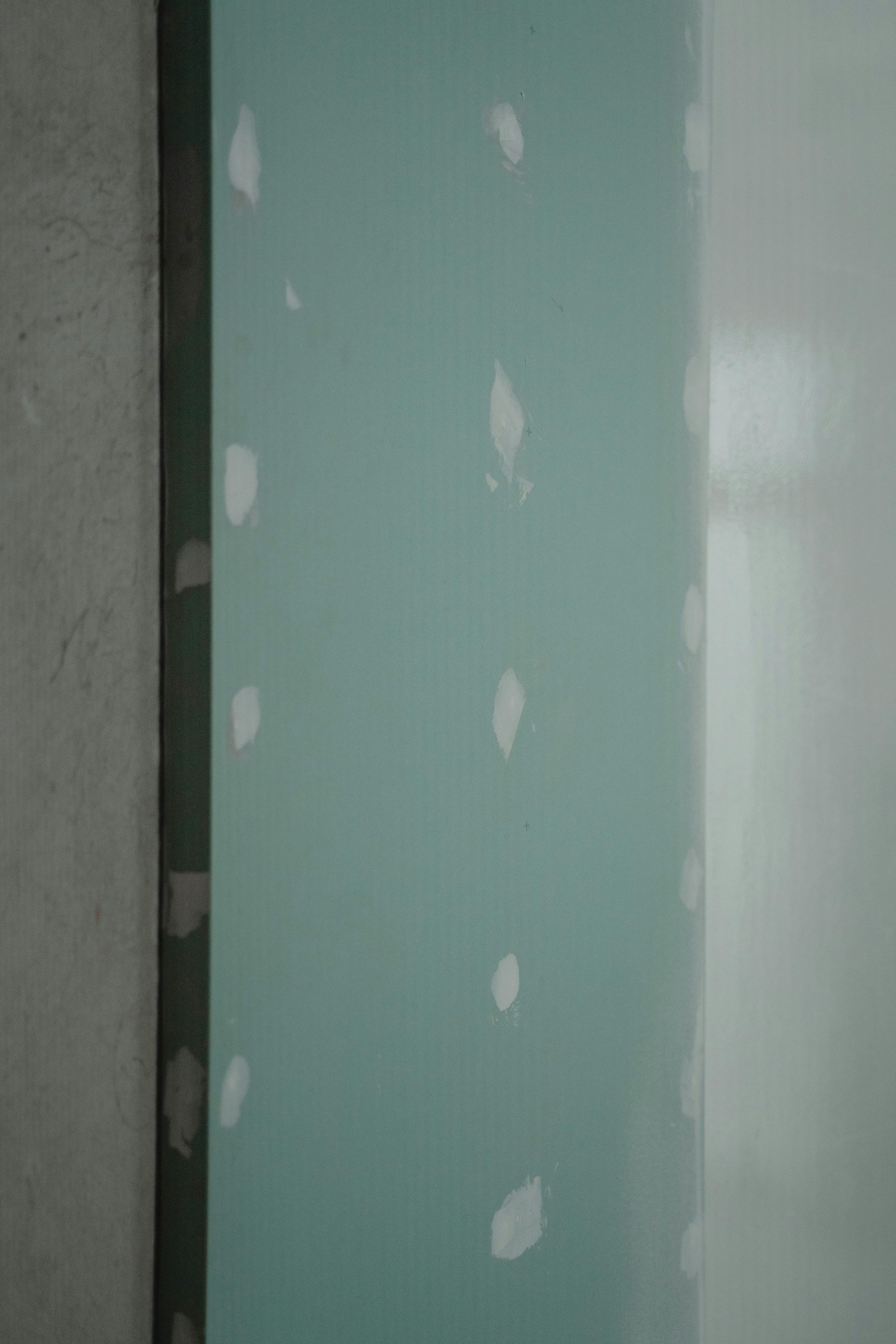 Freshly installed green drywall with white patches, ready for painting or finishing touches in home renovation.
