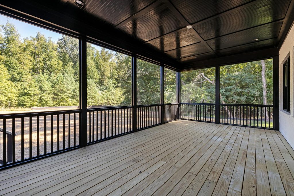 A large wooden deck with a serene view of lush green forest surroundings.